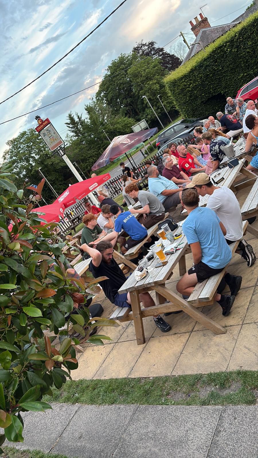 The pub garden full of people at wooden tables under parasols on a bright day
